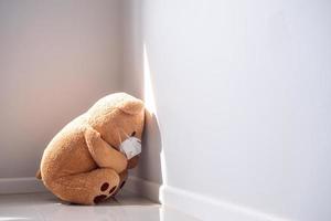 concepto infantil de tristeza. oso de peluche con máscara sentado solo contra la pared de la casa, se ve triste y decepcionado. foto