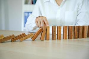 insurance with hands protect a house. The wooden domino block is about to fall on the house. Home insurance or house insurance concept photo