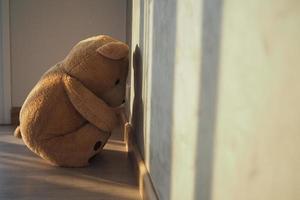 Child concept of sorrow. Teddy bear sitting leaning against the wall of the house alone, look sad and disappointed. photo