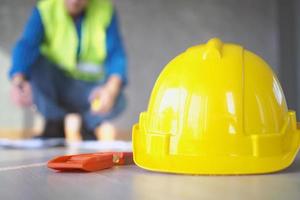 Focus on the yellow hat and the water level placed on the floor. The back has a look at the data that is placed. photo