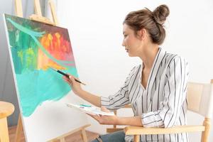 la artista femenina profesional usa pincel en el arte abstracto para crear una obra maestra. pintura de pintor con acuarelas o aceite en casa de estudio. bella mujer disfruta pintando como hobby. recreación laboral foto
