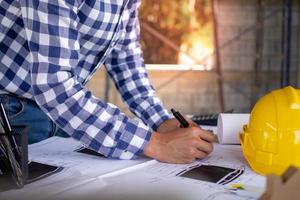 el primer plano de la mano del ingeniero está dibujando un plan impreso con equipo, de pie en los escritorios y planificando la construcción de casas o apartamentos.