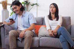 The wife is suspicious of the husband while the husband is sitting on the phone. photo