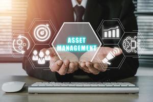 Asset management Business technology internet concept, Businessman hand holding virtual screen asset management icon on office desk workplace. photo