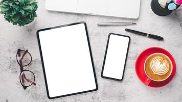 Office desk workplace with blank screen tablet and smart phone, laptop, pen, eyeglass and cup of coffee, Top view flat lay. photo