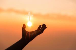 Faith of christian concept. Spiritual prayer hands over sun shine with blurred beautiful sunset background. Female hands worship God with love and faith. silhouette of a woman praying with a cross.