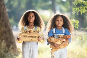 Two black girls hold a brown chicken in their embrace of love with their eyes closed. A little black girl is holding a hen in a farm. photo