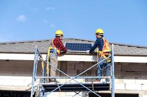 un equipo de técnicos asiáticos instala paneles solares en el techo de una casa. vista transversal del constructor en casco instalando el concepto de sistema de panel solar de energía renovable foto