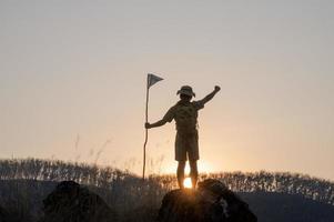 silueta de los boy scouts de América sosteniendo la bandera en la cima de la montaña con cielo azul y luz solar. simboliza el liderazgo de los scouts en el trekking que logra sus metas y objetivos. foto