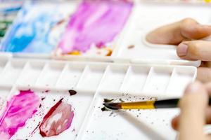 manos de primer plano sosteniendo pincel y paleta de colores con pinturas de acuarela de pintura de artista foto