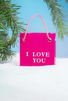 Pink package with text I love you, stands on snow with fir branches. Valentine's, International Women's and Mother's Day, March 8, birthday, shopping. Copy space photo