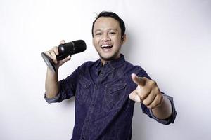 Portrait of carefree Asian man, having fun karaoke, singing in microphone while standing over white background photo