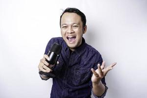 Portrait of carefree Asian man, having fun karaoke, singing in microphone while standing over white background photo