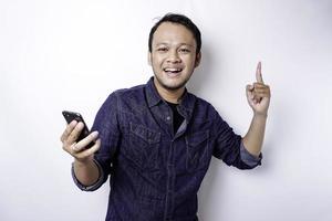 A portrait of a happy Asian man wearing a blue shirt and holding her phone, isolated by white background photo