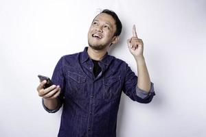 un retrato de un hombre asiático feliz con una camisa azul y sosteniendo su teléfono, aislado por un fondo blanco foto