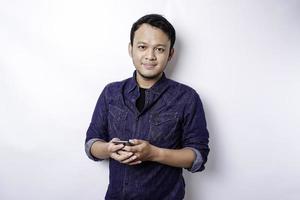 Excited Asian man wearing blue shirt smiling while holding his phone, isolated by white background photo