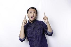 Shocked Asian man wearing blue shirt pointing at the copy space on top of him, isolated by white background photo