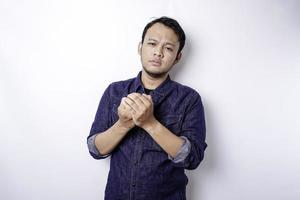 Calm spiritual handsome Asian guy praying with closed eyes. Serious peaceful young man with joining hands meditating. Belief concept photo