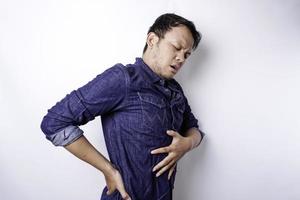 Tired upset young man wears blue shirt suffering from pain, muscle spasm at workplace. Fatigue, deadline, pain and incorrect posture photo