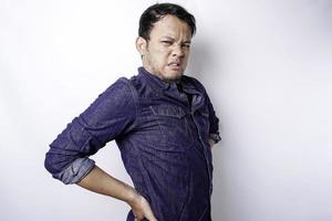 Tired upset young man wears blue shirt suffering from pain, muscle spasm at workplace. Fatigue, deadline, pain and incorrect posture photo