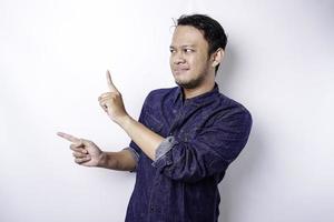 Excited Asian man wearing blue shirt pointing at the copy space beside him, isolated by white background photo