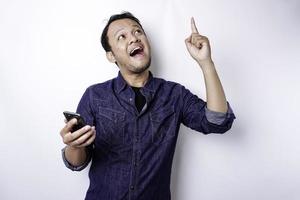 A portrait of a happy Asian man wearing a blue shirt and holding her phone, isolated by white background photo