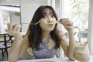 Mujer asiática joven divertida que come la pasta sabrosa en café foto