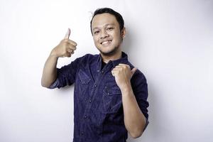 Excited Asian man wearing blue shirt pointing at the copy space beside him, isolated by white background photo