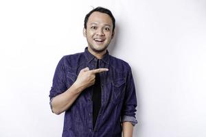 Excited Asian man wearing blue shirt pointing at the copy space beside him, isolated by white background photo