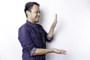 Excited Asian man wearing blue shirt pointing at the copy space beside him, isolated by white background photo