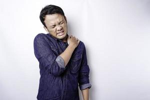 Tired upset young man wears blue shirt suffering from pain, muscle spasm at workplace. Fatigue, deadline, pain and incorrect posture photo