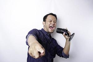 Portrait of carefree Asian man, having fun karaoke, singing in microphone while standing over white background photo