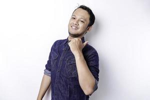 Excited Asian man wearing blue shirt pointing at the copy space beside him, isolated by white background photo