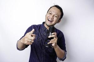 retrato de un hombre asiático despreocupado, divirtiéndose en el karaoke, cantando en el micrófono mientras está de pie sobre fondo blanco
