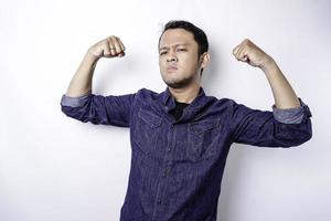 hombre asiático emocionado con una camisa azul que muestra un gesto fuerte levantando los brazos y los músculos sonriendo con orgullo foto