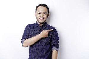 Excited Asian man wearing blue shirt pointing at the copy space beside him, isolated by white background photo