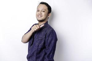 Excited Asian man wearing blue shirt pointing at the copy space beside him, isolated by white background photo