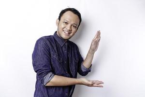 Excited Asian man wearing blue shirt pointing at the copy space beside him, isolated by white background photo