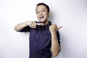 Excited Asian man wearing blue shirt pointing at the copy space beside him, isolated by white background photo