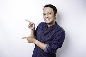 Excited Asian man wearing blue shirt pointing at the copy space beside him, isolated by white background photo