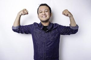 Excited Asian man wearing a blue shirt showing strong gesture by lifting his arms and muscles smiling proudly photo