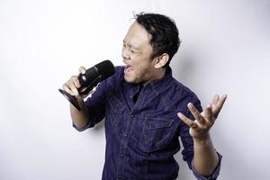 retrato de un hombre asiático despreocupado, divirtiéndose en el karaoke, cantando en el micrófono mientras está de pie sobre fondo blanco