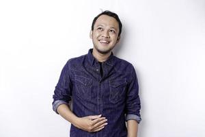 An Asian man is hungry and touching his belly while looking aside thinking what to eat, isolated by white background photo