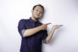 Excited Asian man wearing blue shirt pointing at the copy space beside him, isolated by white background photo