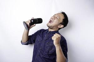 Portrait of carefree Asian man, having fun karaoke, singing in microphone while standing over white background photo