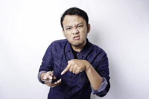 The angry and mad face of Asian man in blue shirt holding his phone isolated white background. photo