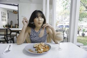 Mujer asiática joven divertida que come la pasta sabrosa en café foto