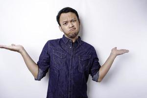 A portrait of an Asian man wearing a blue shirt looks so confused between choices, isolated by a white background photo