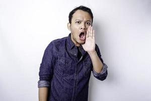 Young handsome man wearing a blue shirt shouting and screaming loud with a hand on his mouth. communication concept. photo