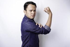 Excited Asian man wearing a blue shirt showing strong gesture by lifting his arms and muscles smiling proudly photo